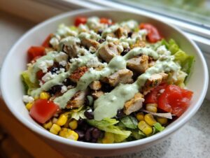 Close-up of a vibrant southwest salad bowl featuring grilled chicken, corn, black beans, tomatoes, and creamy green dressing.