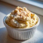 A close-up of fluffy, whipped cinnamon butter topped with extra cinnamon spice in a small white ramekin.