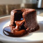 Close-up of a rich chocolate lava cake with molten center oozing onto a white plate.