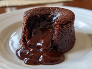 Close-up of a single chocolate lava cake with molten chocolate oozing out onto a white plate.