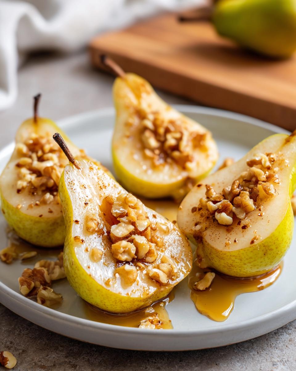 Four halves of glistening baked pears topped with chopped walnuts and drizzled with syrup on a light plate.