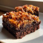 A rich, fudgy German chocolate brownie square topped with a glistening, caramelized coconut and pecan frosting.