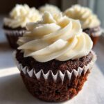 A close-up of one dark, rich gingerbread cupcake topped with a swirl of creamy white frosting.