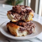 Two gooey chocolate cinnamon rolls stacked, showing the soft interior and thick chocolate frosting.