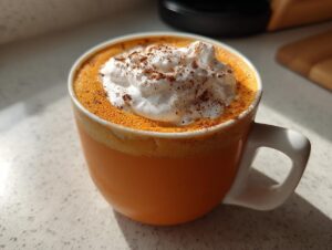 Close-up of a homemade pumpkin spice latte topped with whipped cream and cinnamon in an orange mug.