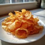 A close-up of a mound of crispy, seasoned potato chips piled high on a white plate.