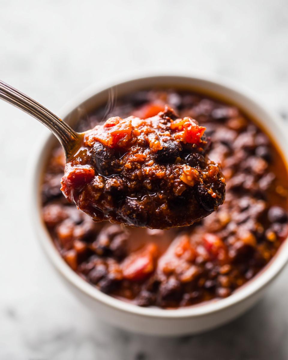 A spoonful of thick, steaming black bean chili being lifted from a white bowl.