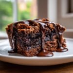 Close-up of a rich slice of hot fudge brownie bread covered in glossy, dripping hot fudge sauce.
