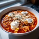 A close-up of a bowl of rich instant pot lasagna soup, topped with dollops of ricotta cheese, shredded mozzarella, and herbs.
