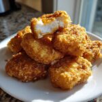 A close-up pile of golden brown homemade chicken nuggets, with one nugget broken open showing juicy white meat inside.