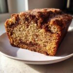 Close-up of a moist slice of snickerdoodle zucchini bread with a visible cinnamon swirl and sugary topping.
