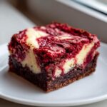 A single square of rich red velvet cheesecake brownies featuring a dark chocolate base and a vibrant red and cream cheese swirl topping.