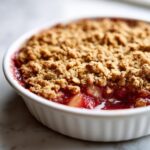 Close-up of a bubbling, freshly baked rhubarb crisp topped with a golden, crunchy oat topping in a white ramekin.