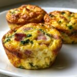 Three baked egg bites made with egg, bacon, and spinach, served on a white plate.