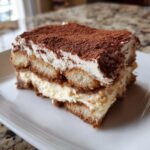 A perfect slice of layered tiramisu recipe featuring ladyfingers, creamy filling, and a heavy dusting of cocoa powder.