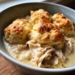 A close-up view of a bowl filled with creamy slow cooker chicken and dumplings, featuring shredded chicken and golden-brown biscuits.