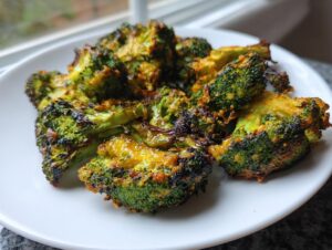Close-up of perfectly roasted and slightly charred smashed broccoli florets coated in seasoning on a white plate.