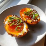 Two halves of soft-boiled marinated eggs with jammy yolks, topped with sesame seeds and green onions.