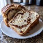 A loaf of soft raisin bread sliced, showing a rich swirl of cinnamon and plump raisins throughout the crumb.
