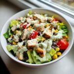 A vibrant bowl of Southwest salad featuring grilled chicken, black beans, corn, tomatoes, and creamy avocado dressing.