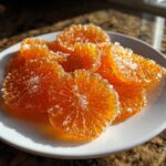 Close-up of glistening candied orange slices heavily coated in sugar crystals served on a white plate.