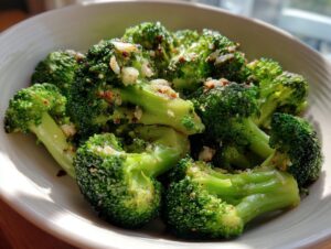 Close-up of bright green steamed broccoli florets seasoned with garlic and red pepper flakes in a white bowl.