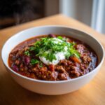 Close-up of a steaming bowl of rich, hearty high protein chili topped with sour cream and fresh parsley.