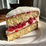 A moist slice of strawberry cake with two layers of yellow sponge, white frosting, and bright red strawberry filling.