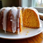 A slice cut from a vibrant orange sweet potato pound cake topped with thick white glaze.