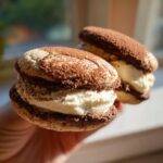 Two homemade tiramisu cookies filled with thick cream and dusted heavily with cocoa powder.