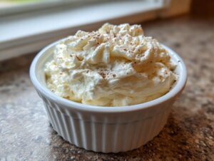 A close-up of freshly whipped cinnamon butter, topped with a dusting of cinnamon, served in a white fluted ramekin.