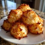 A pile of freshly baked, golden brown coconut macaroons with crispy edges served on a white plate.