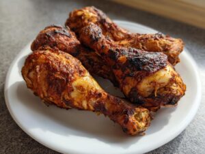 Four crispy, seasoned air fryer chicken legs piled on a white plate, showing a deep golden-brown, slightly charred exterior.