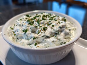 Close-up of a creamy, thick blue cheese dip served in a white bowl and garnished with fresh chopped chives.