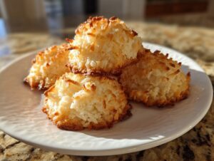 Four golden brown, perfectly baked chewy coconut cookies stacked slightly on a white plate.