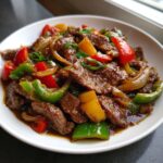 Close-up of amazing chinese pepper steak with colorful bell peppers and onions in a glossy brown sauce.