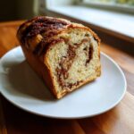 A thick slice of homemade cinnamon bread showing a rich, dark swirl pattern inside the soft dough.