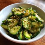 Close-up of vibrant Asian cucumber salad slices tossed in a savory dressing and topped with toasted sesame seeds.