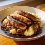 Three browned sausages served over creamy mashed potatoes with rich onion gravy, classic bangers and mash with onion gravy.