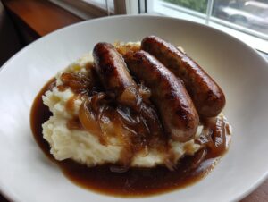 Three browned sausages served over creamy mashed potatoes, topped with caramelized onions and rich onion gravy for bangers and mash.