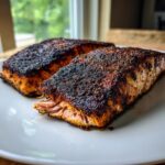 Two perfectly cooked pieces of blackened salmon with a dark, spicy crust resting on a white plate.