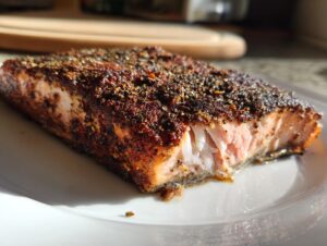 Close-up of a perfectly cooked salmon fillet coated heavily with blackened salmon seasoning on a white plate.