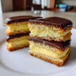 Close-up stack of three boston cream pie cookies showing vanilla cake, pastry cream filling, and chocolate glaze.