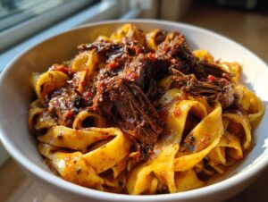Close-up of rich braised short rib pappardelle tossed in a savory red sauce, served in a white bowl.