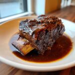 Close-up of a tender, dark braised short ribs dutch oven piece resting in rich brown sauce.
