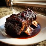 A close-up of a single, deeply colored braised short ribs piece covered in a thick, glossy sauce.