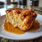 A decadent slice of bread pudding with bourbon sauce generously poured over the top and pooling on the plate.