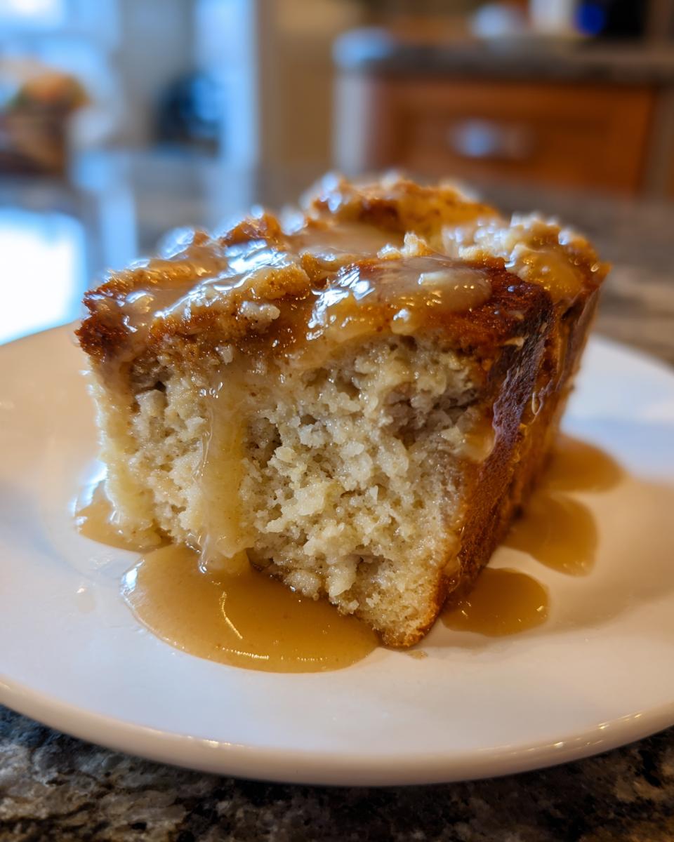 A close-up of a square slice of bread pudding with bourbon sauce generously drizzled over the top and pooling on the white plate.