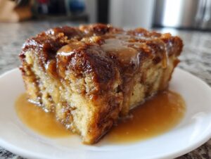 A generous slice of bread pudding with bourbon sauce drizzled over the top and pooling on the white plate.
