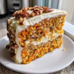 A moist slice of carrot cake with candied pecans on top and cream cheese frosting.
